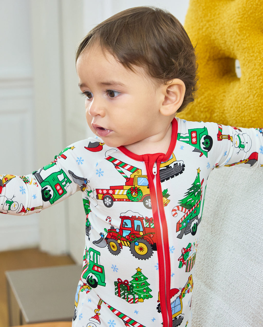 Front view of a child wearing the Merry Truckmas Bamboo Zippy, showing its red neckline, zipper and festive vehicle print.