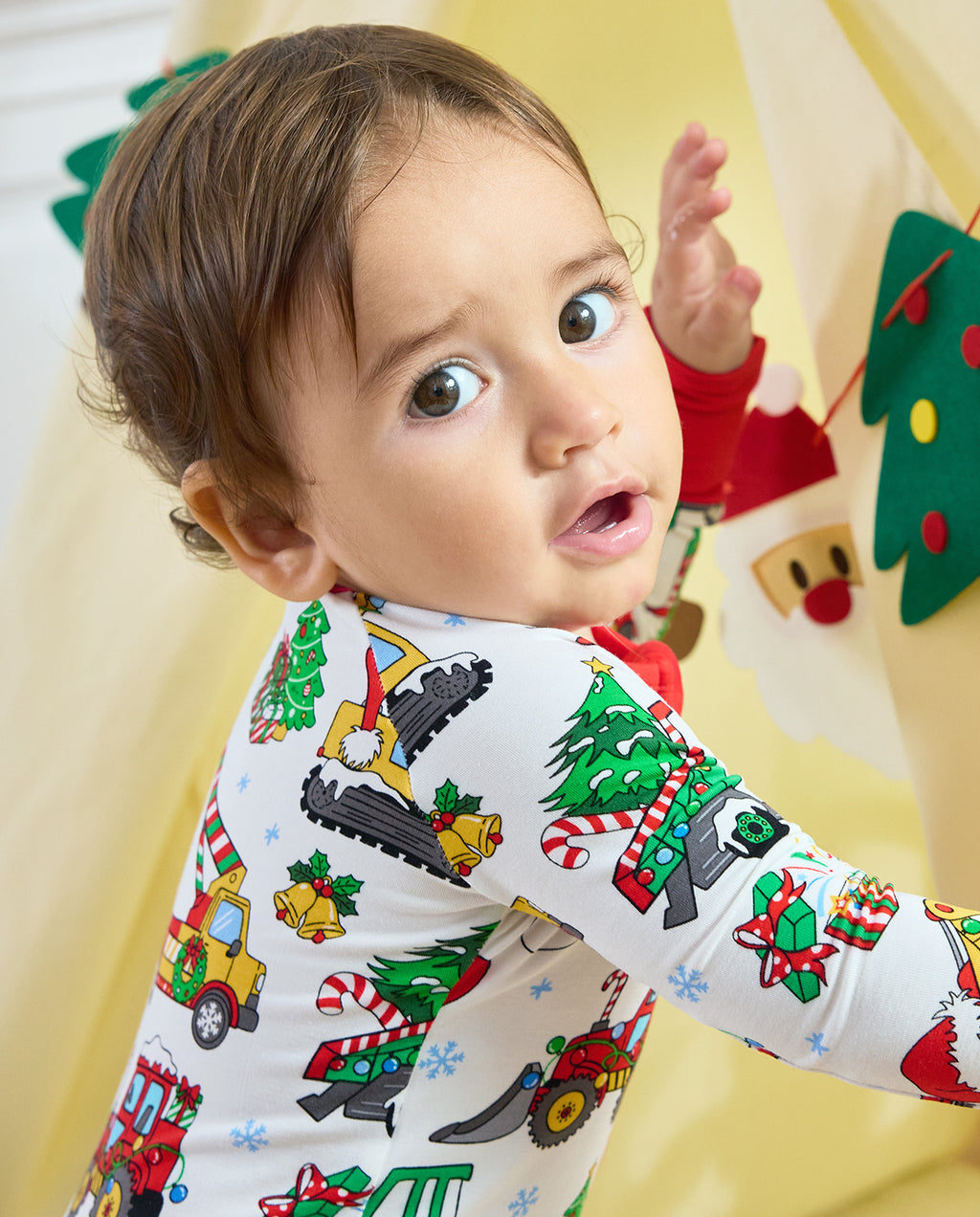 Child looking over one shoulder in the Merry Truckmas Bamboo Zippy, showing Christmas trees and construction vehicles across the sleeve and back.