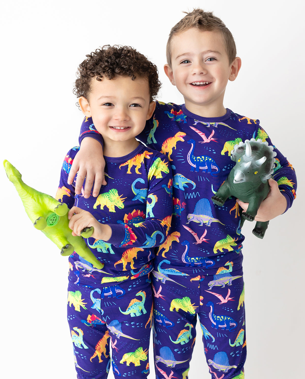 Two children seated with toy dinosaurs in Neo Dino pajamas