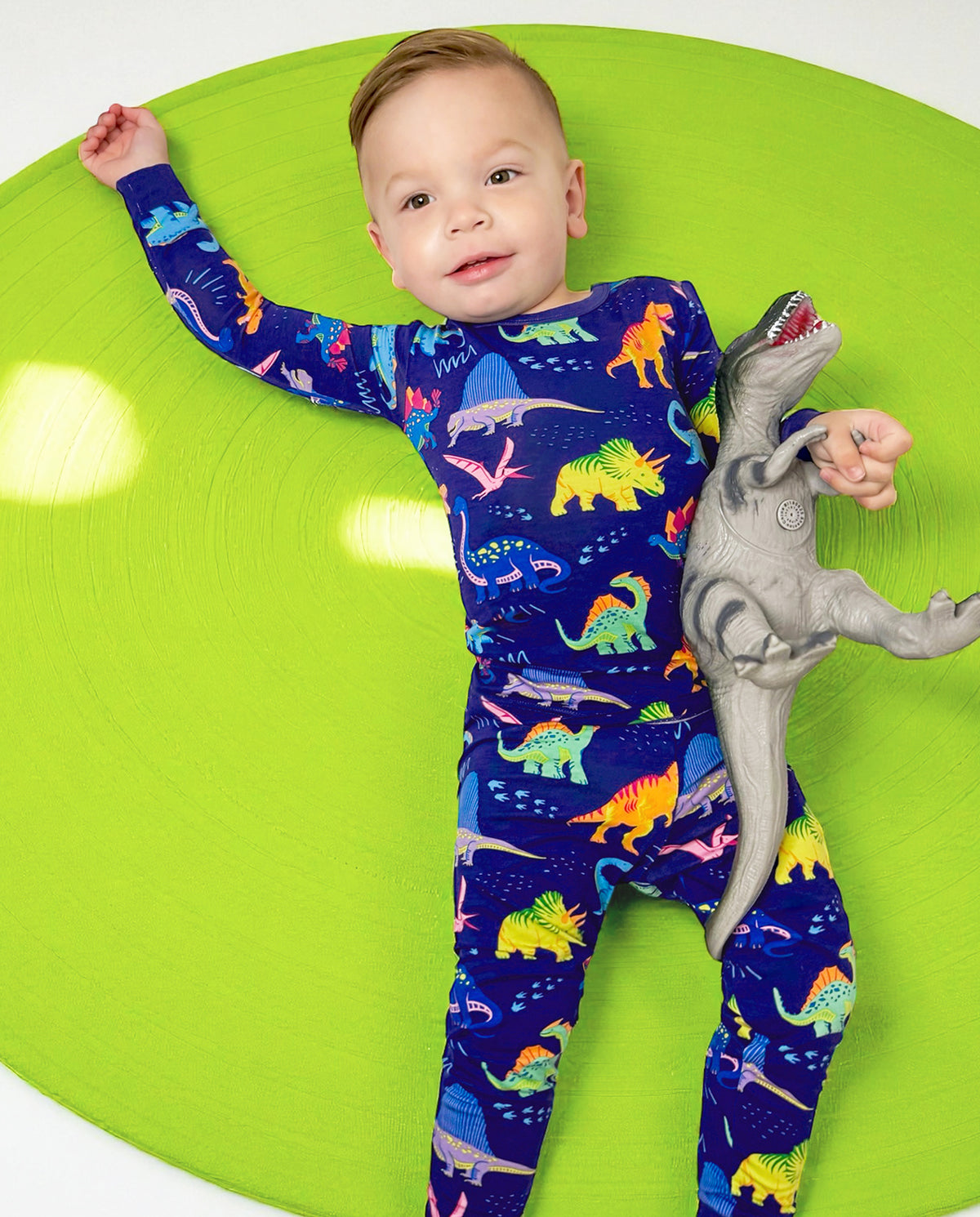 Baby reclining on a green seat in Neo Dino pajamas