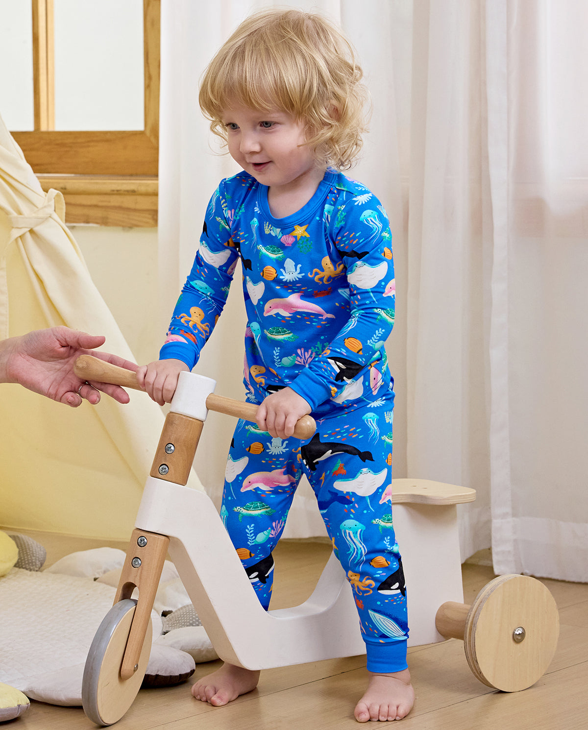 Child holding an adult hand beside a wooden toy in blue pajamas