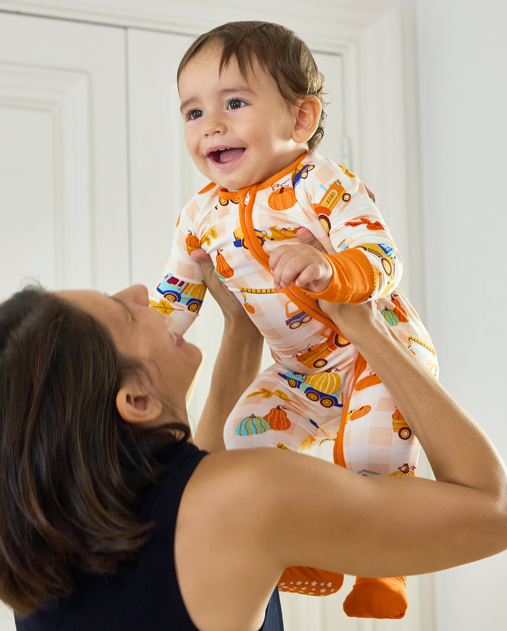 Baby being lifted while wearing Pumpkin Tractors Bamboo Zippy with pumpkins and colorful construction vehicles.