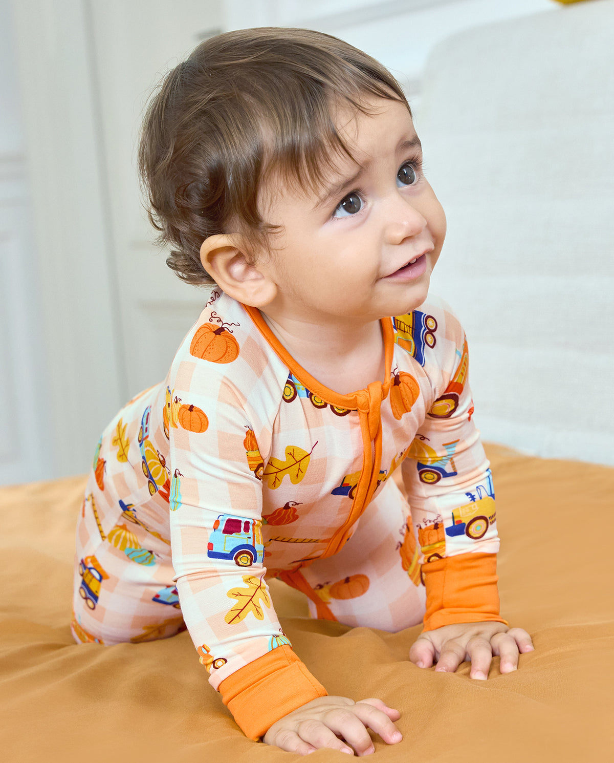 Baby crawling in Pumpkin Tractors Bamboo Zippy with orange cuffs and a pumpkin and vehicle print.