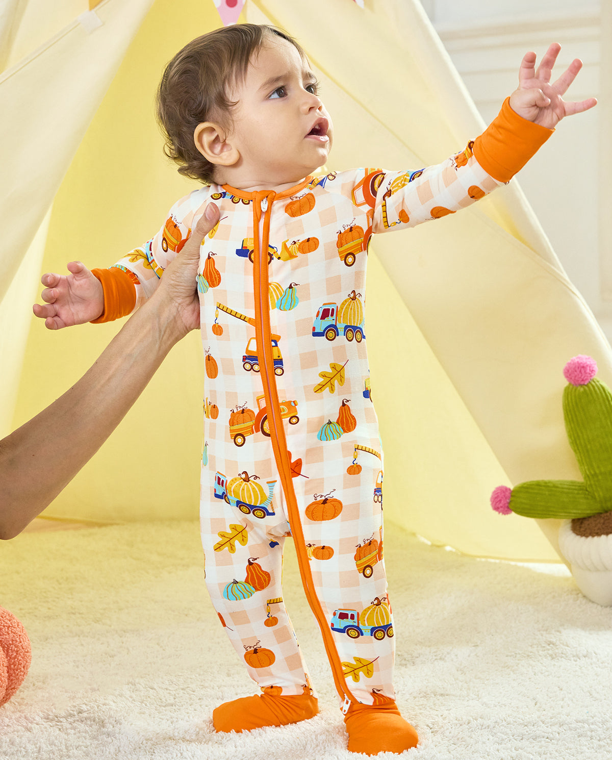 Front view of a baby standing in Pumpkin Tractors Bamboo Zippy with orange cuffs and a two-way zipper.