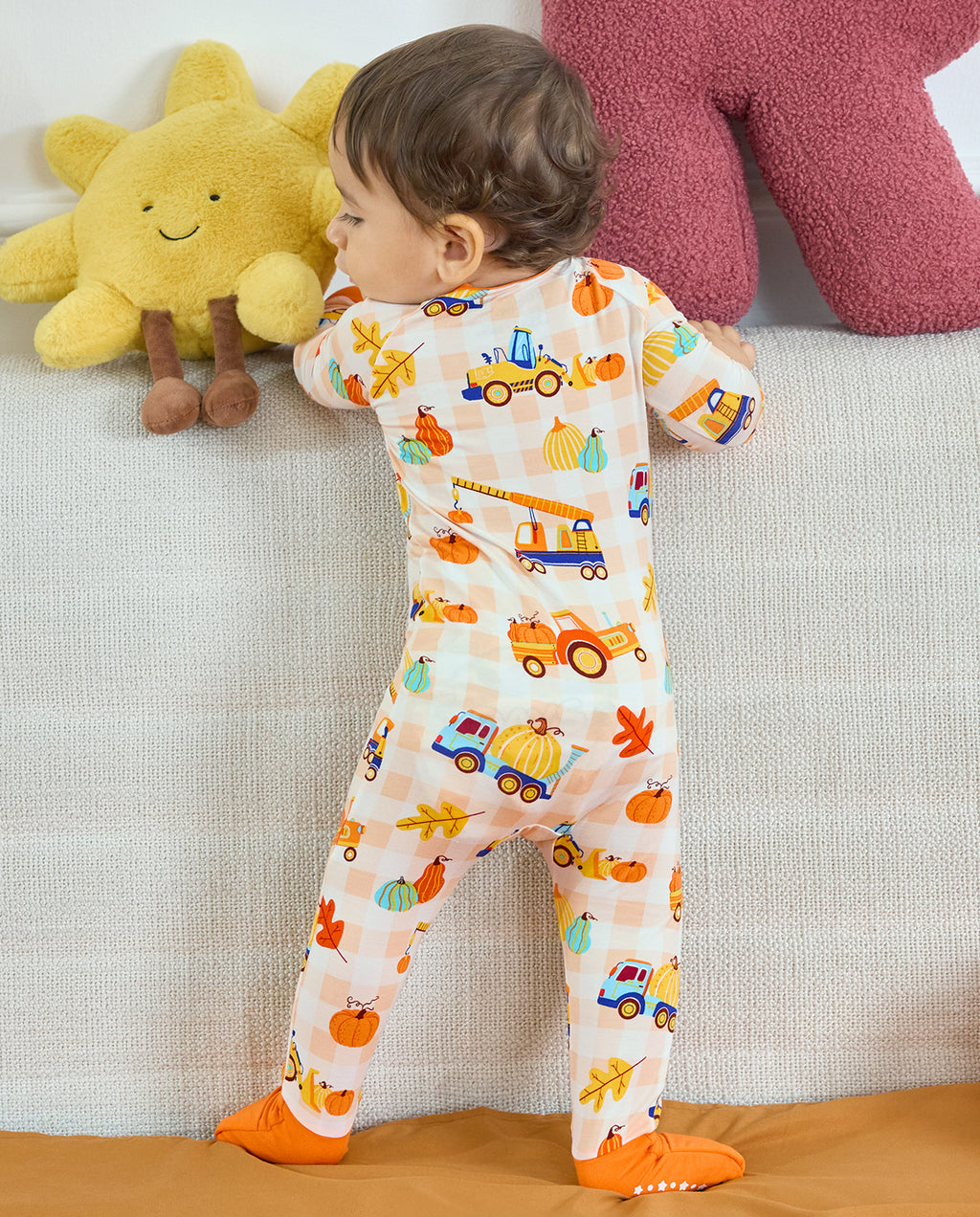 Full back view of Pumpkin Tractors Bamboo Zippy on a baby standing beside a sofa.