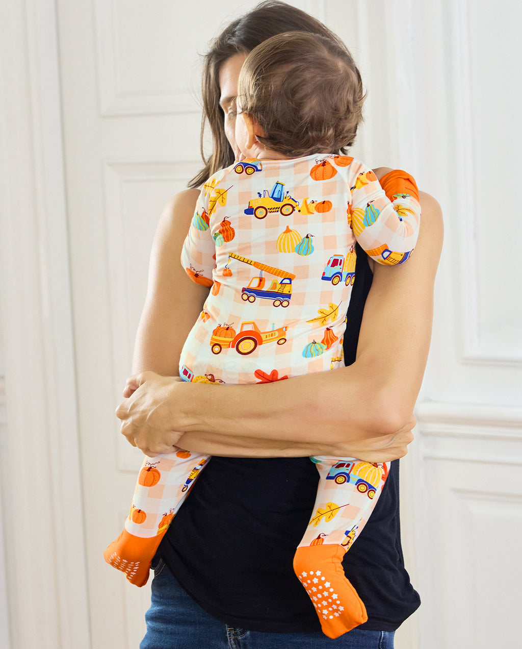 Back view of a baby being held in Pumpkin Tractors Bamboo Zippy with orange foot cuffs.