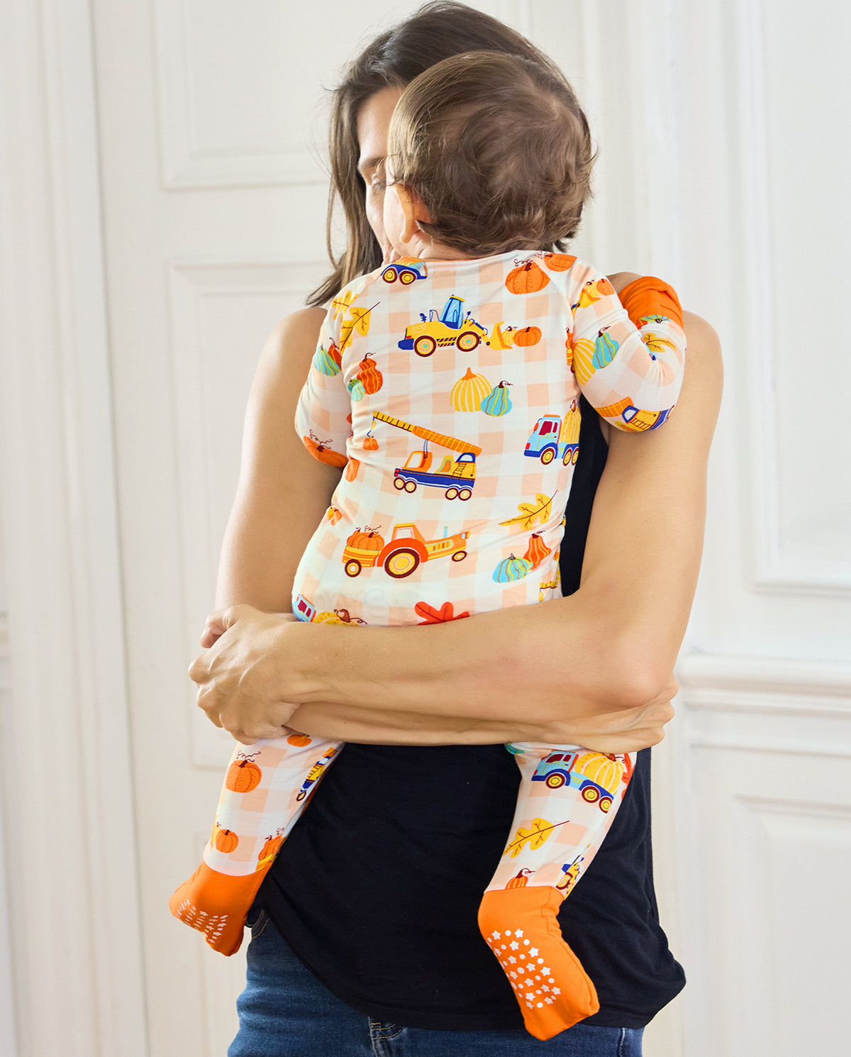 Back view of a baby being held in Pumpkin Tractors Bamboo Zippy with orange foot cuffs.