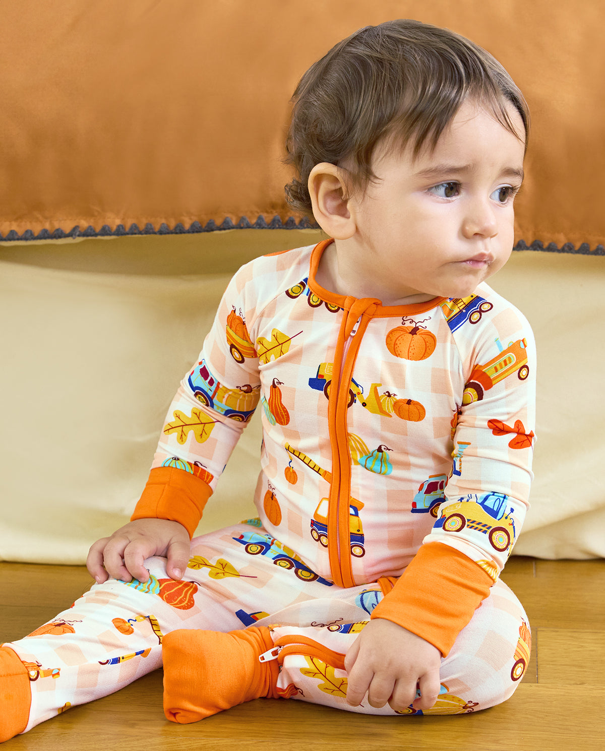 Baby sitting on a sofa in Pumpkin Tractors Bamboo Zippy with orange trim and autumn print.