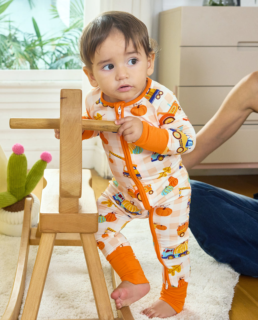 Baby standing beside a wooden toy in Pumpkin Tractors Bamboo Zippy with the orange zipper visible.