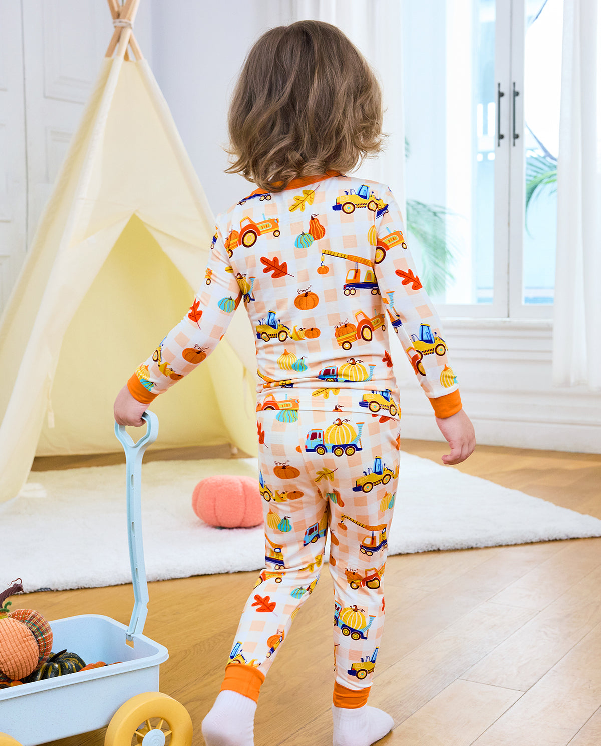 Back view of a child in Pumpkin Tractors long two-piece pajamas near a toy wagon.