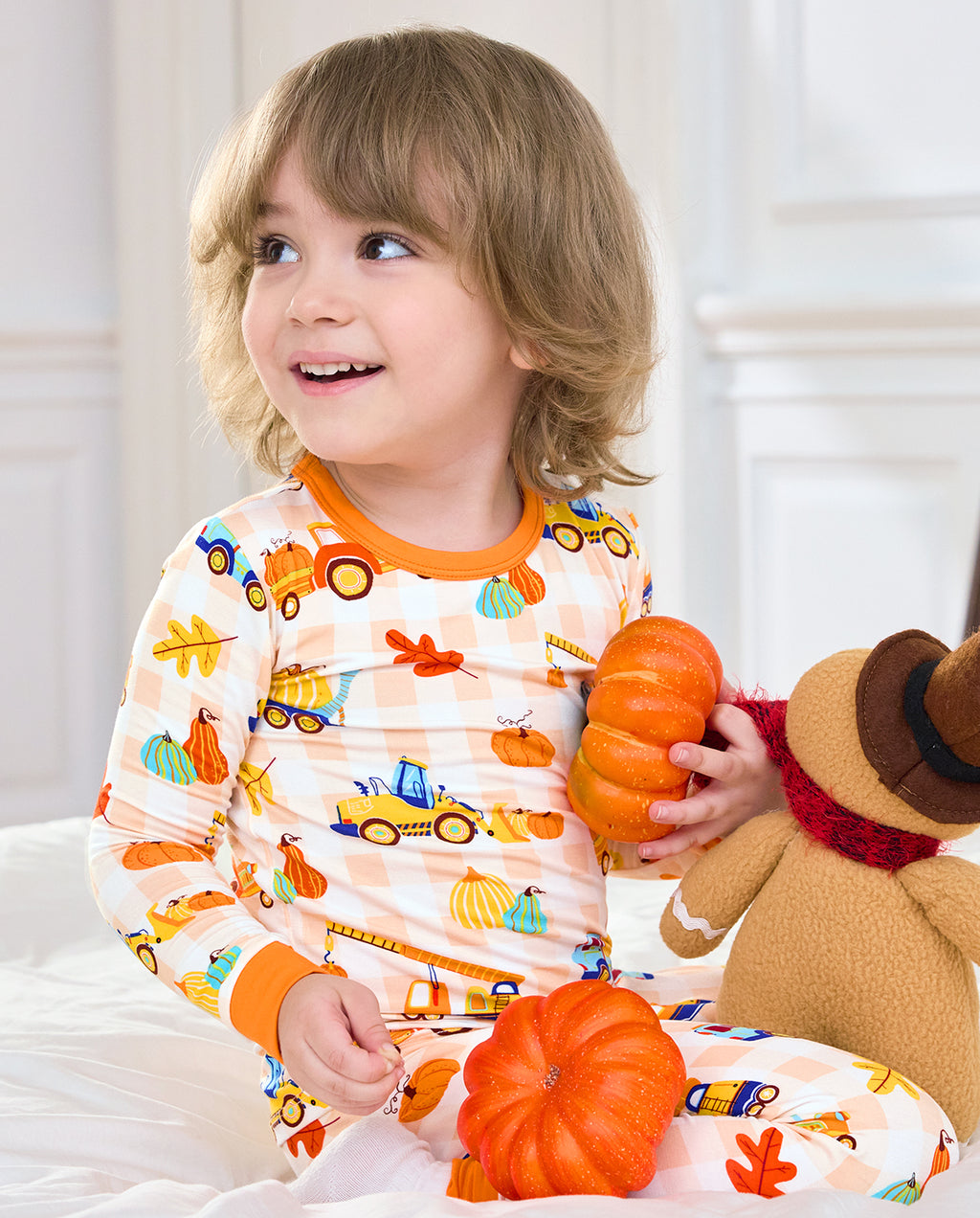 Child wearing Pumpkin Tractors long two-piece pajamas while holding a pumpkin and plush scarecrow.