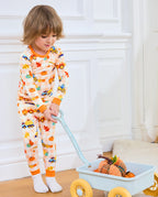 Child wearing Pumpkin Tractors long two-piece pajamas beside a toy wagon with pumpkins.