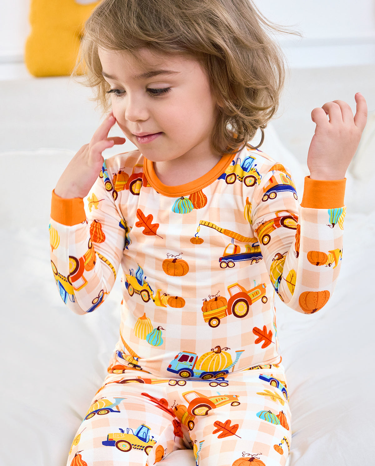 Child seated in Pumpkin Tractors long two-piece pajamas with orange trim.