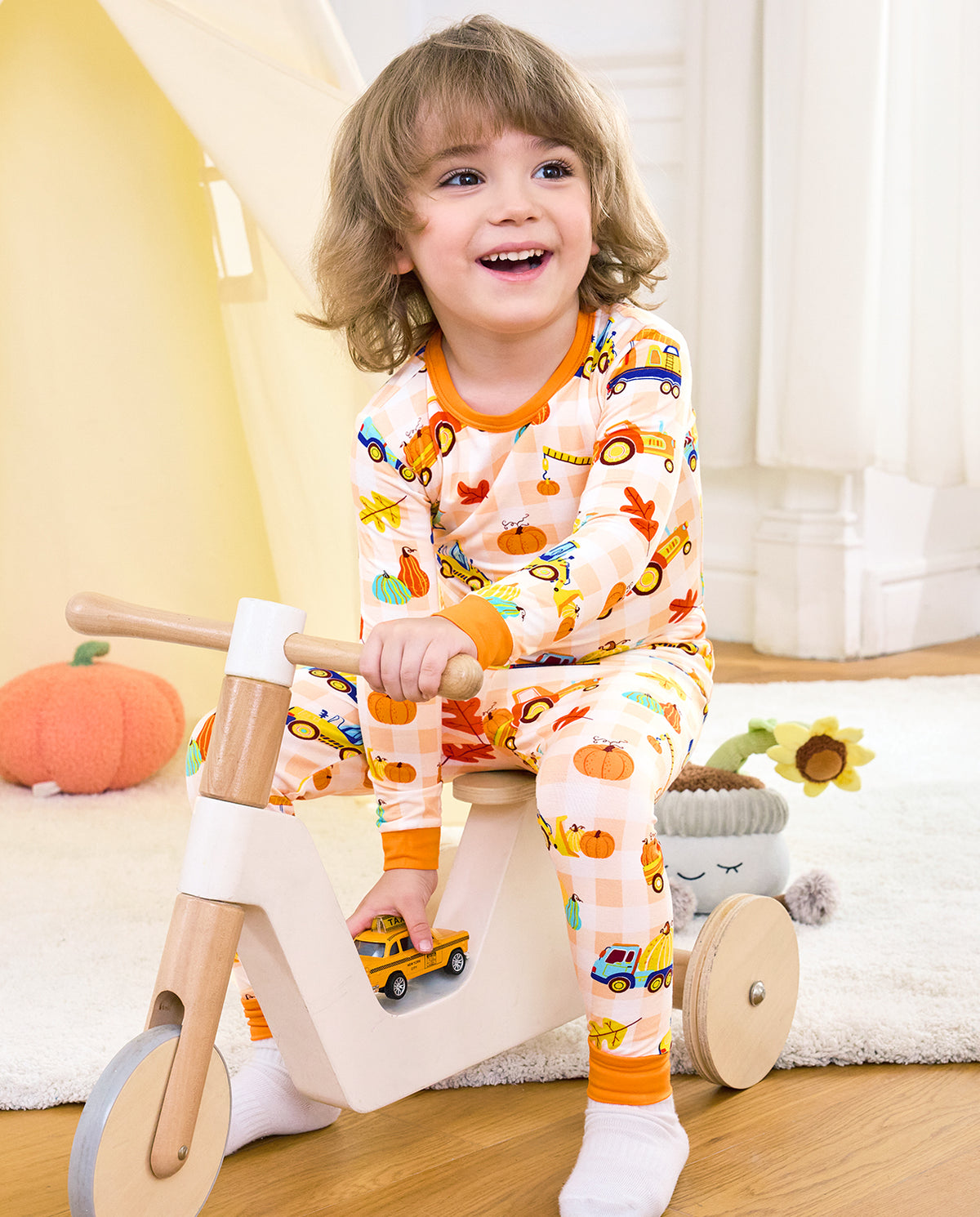 Child wearing Pumpkin Tractors long two-piece pajamas on a wooden toy tricycle.