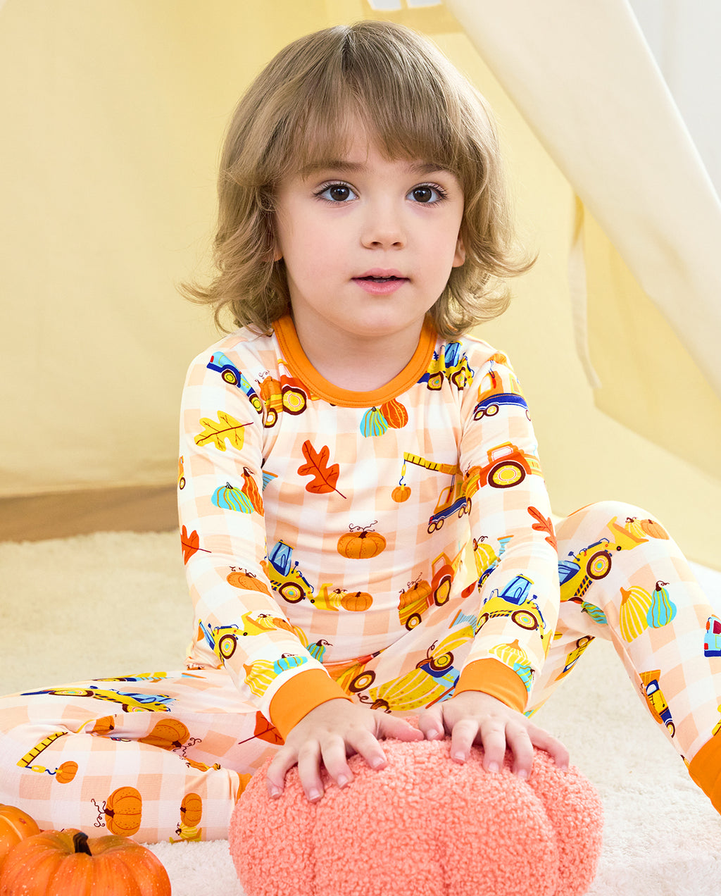 Child wearing Pumpkin Tractors long two-piece pajamas beside a plush pumpkin.