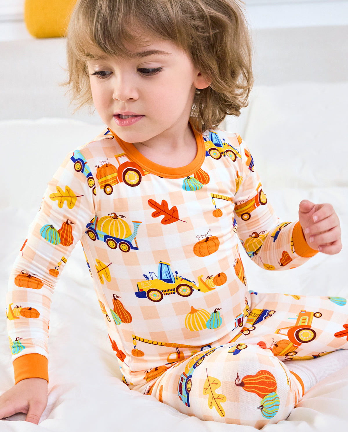 Child wearing Pumpkin Tractors long two-piece pajamas in a bedroom setting.