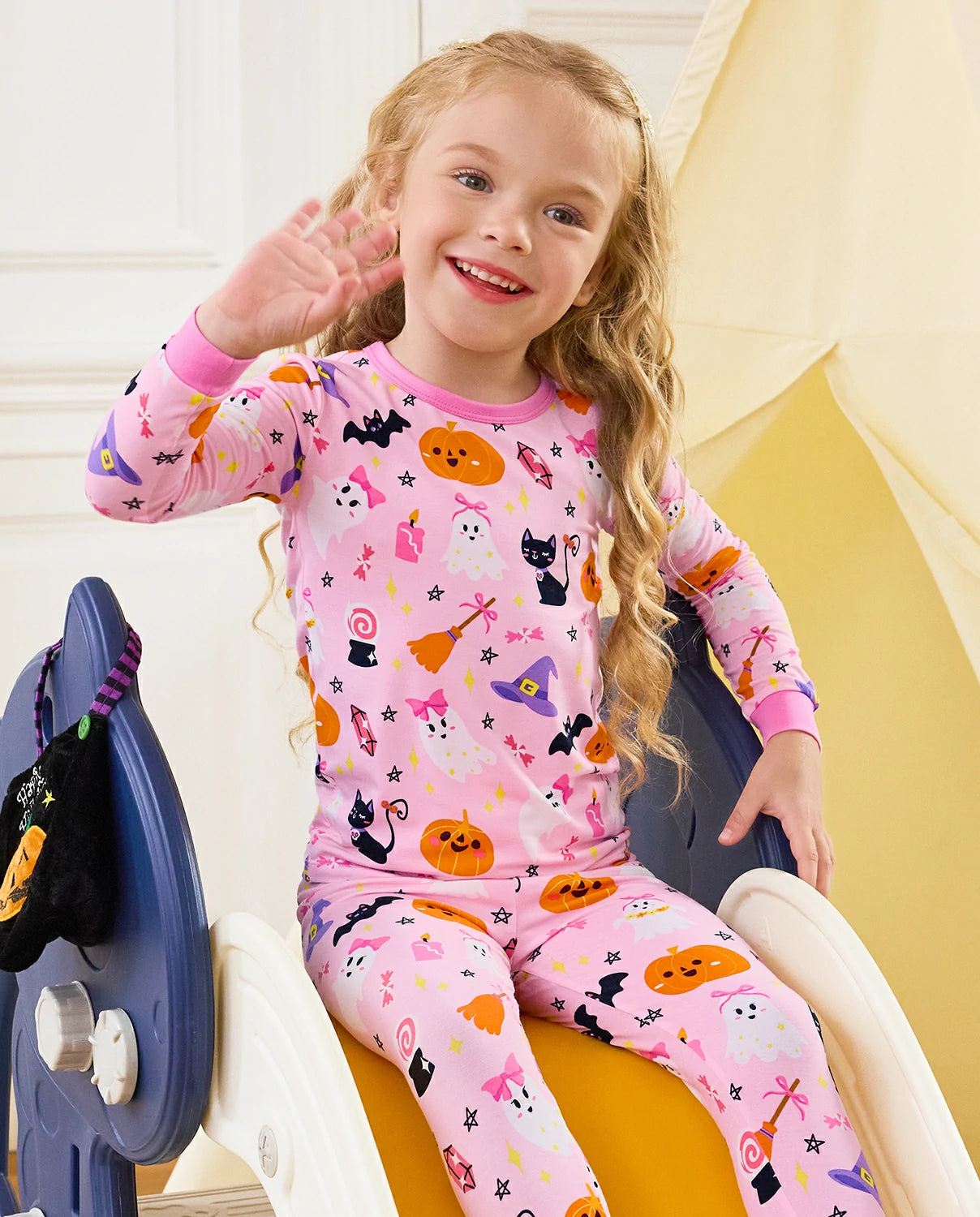 Spooky Cute Long Two-Piece Pajama Set - child wearing the pink Halloween pajamas while seated and waving
