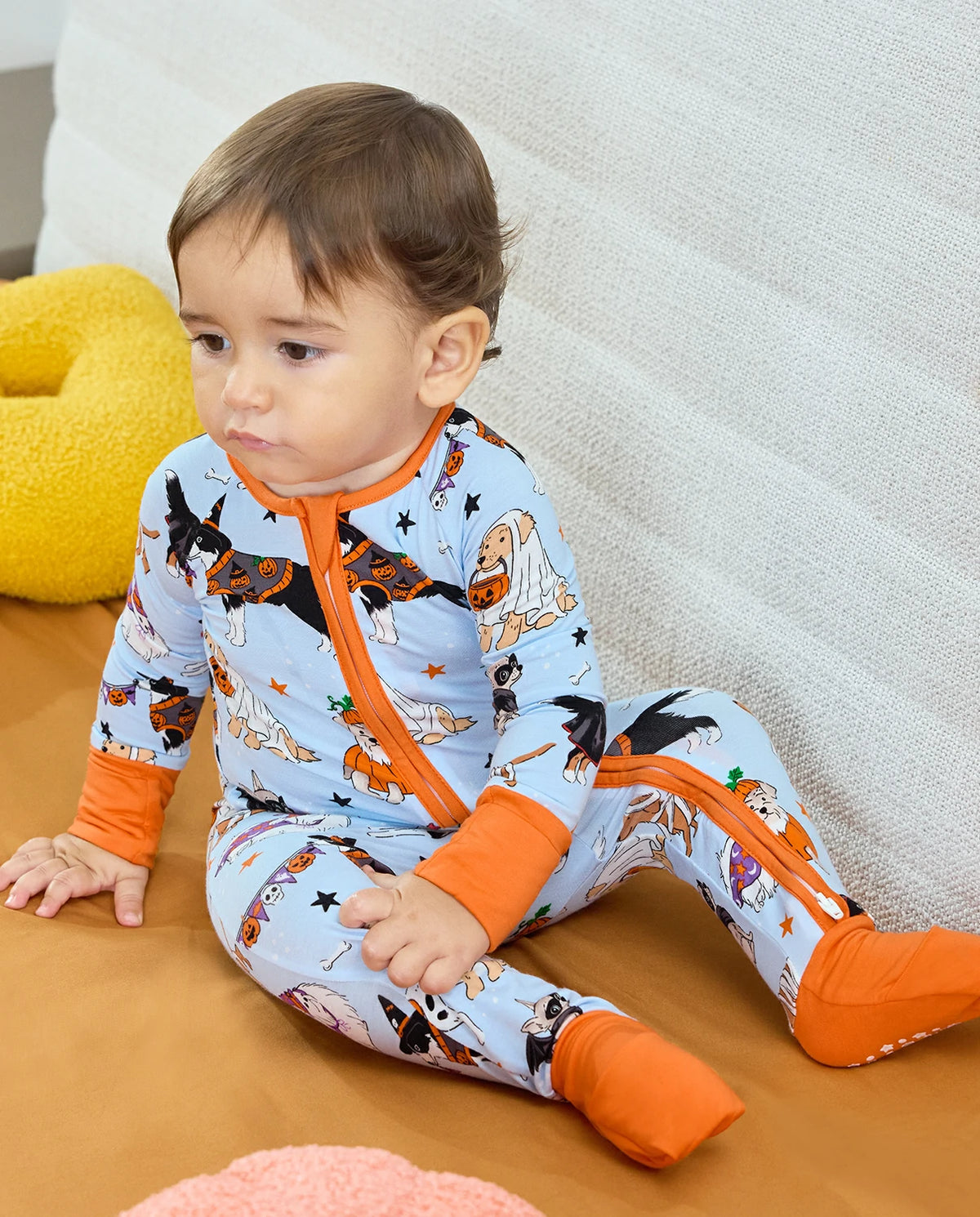 Baby sitting in Spooky Pups Bamboo Zippy on orange blanket