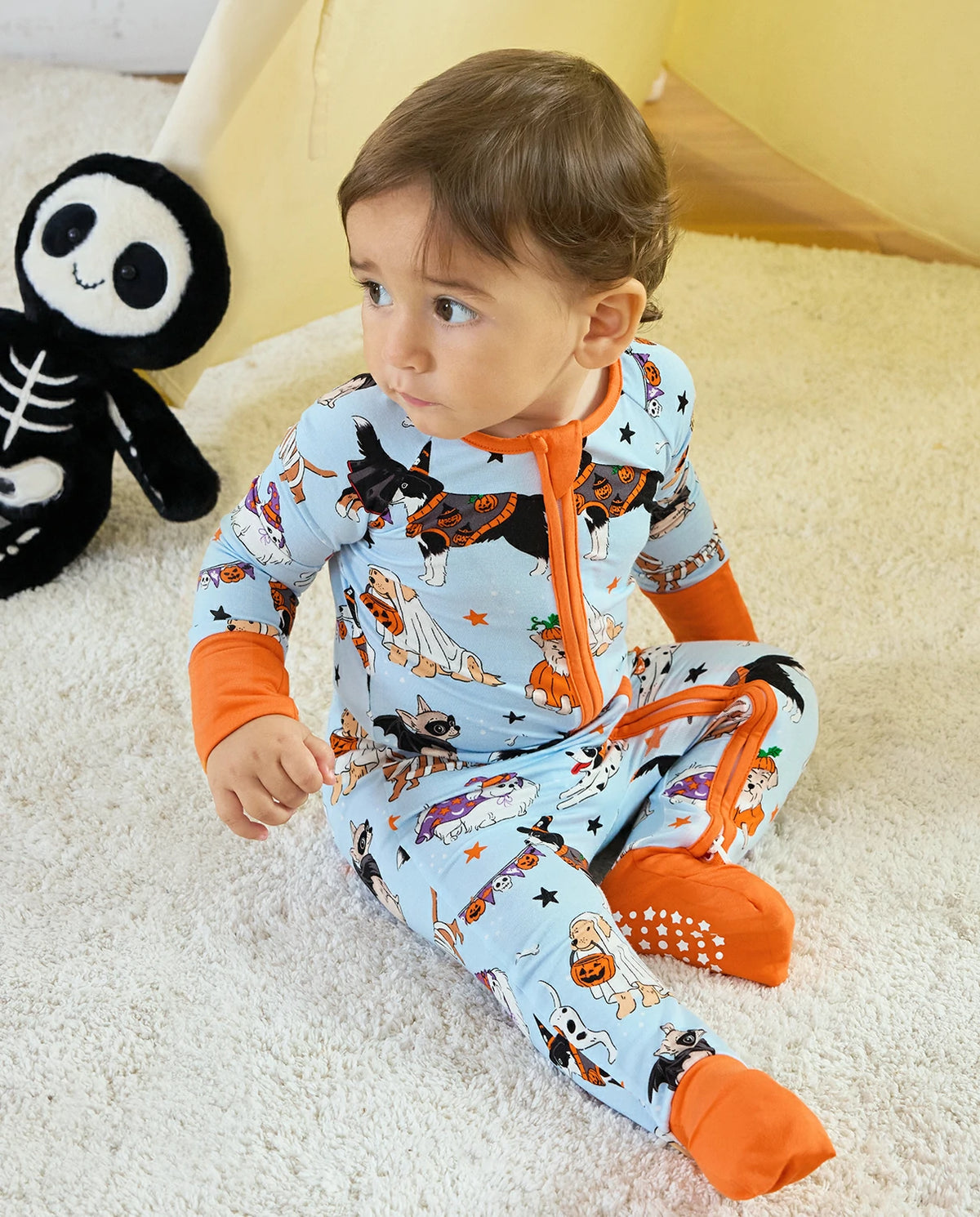 Baby sitting in Spooky Pups Bamboo Zippy with Halloween plush toy nearby
