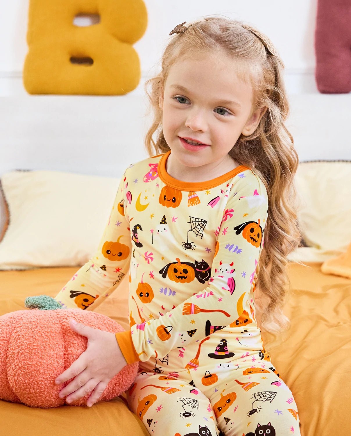 Spooky Sweet Long Two-Piece Pajama Set - child wearing the pajamas while seated with a plush pumpkin