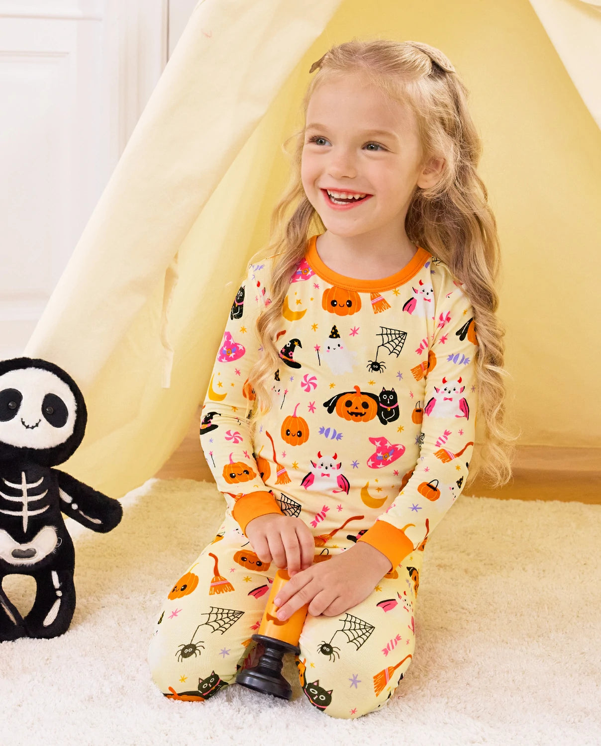 Spooky Sweet Long Two-Piece Pajama Set - child wearing the pajamas while seated beside a skeleton toy