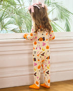 A child wearing a spooky sweet bamboo  footed sleeper with orange socks, standing by a window with palm leaves visible outside.