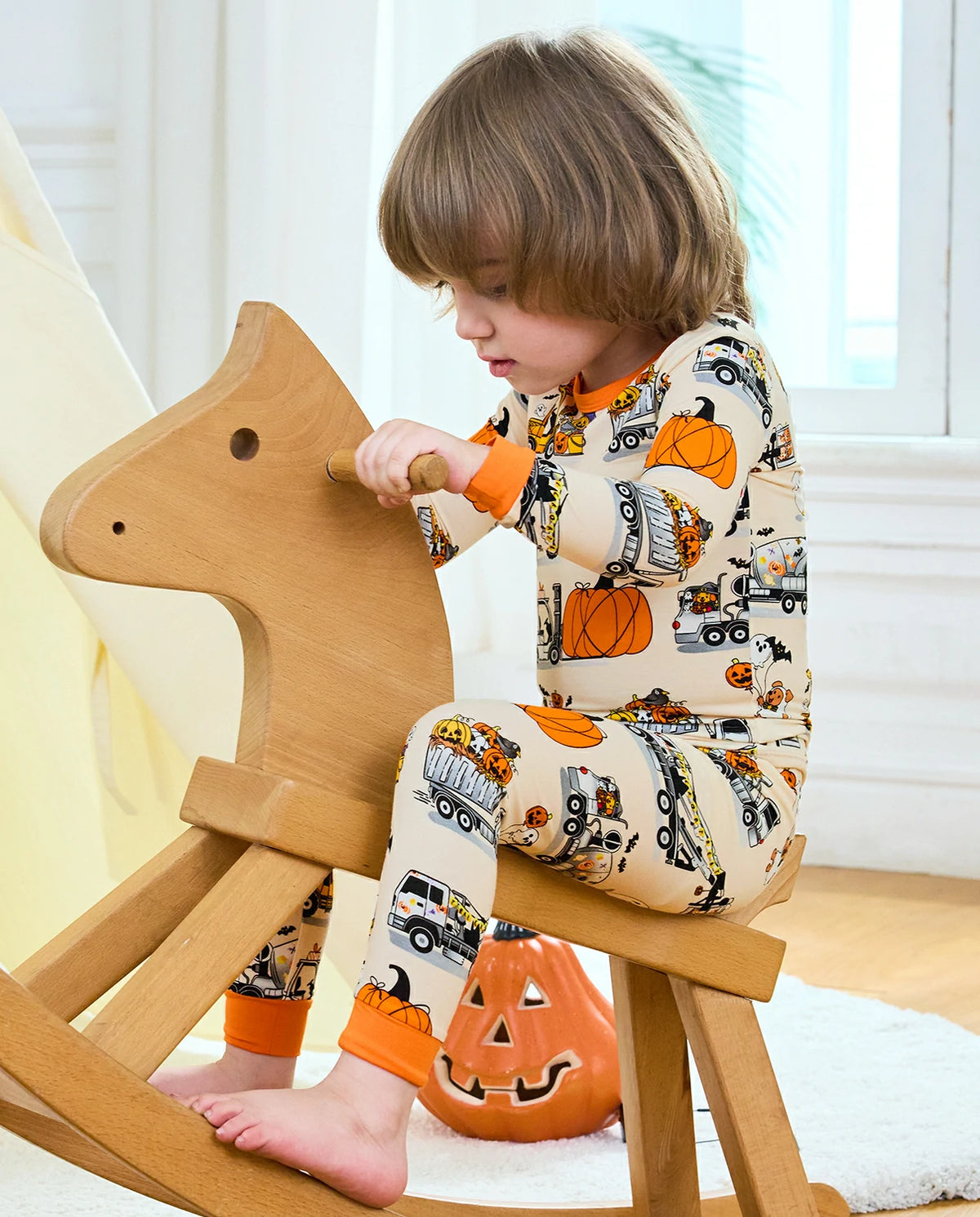 Trick Trucks Long Two-Piece Pajama Set - child wearing the pajamas while seated on a rocking horse