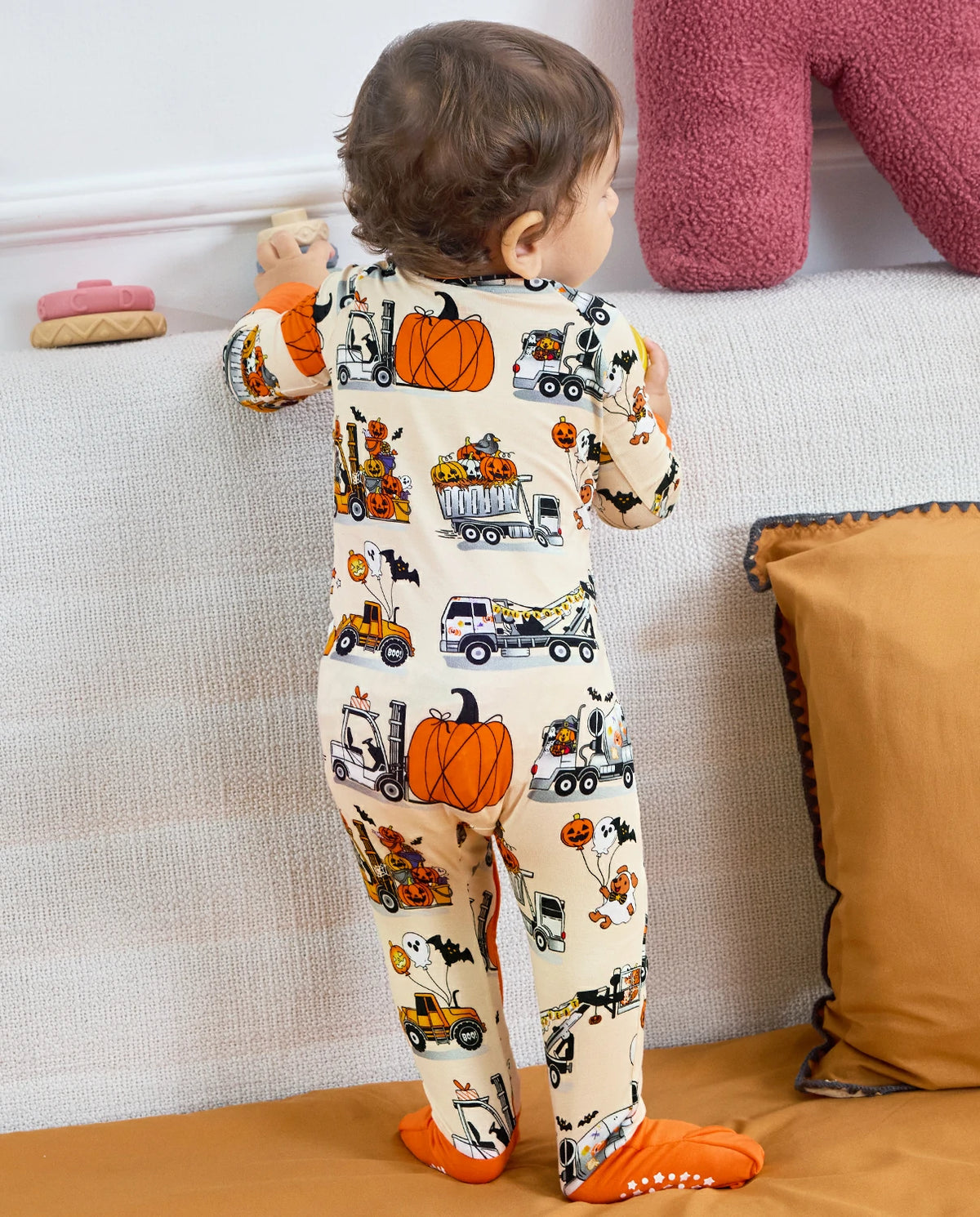 Back view of baby standing in Trick Trucks bamboo zippy with orange footies