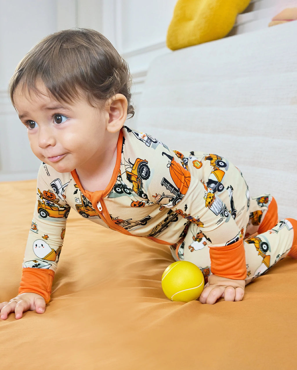 Baby crawling in Trick Trucks bamboo zippy with orange cuffs and Halloween trucks